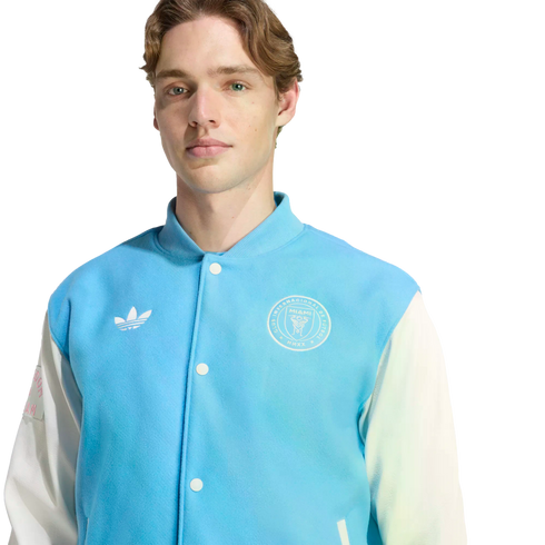 A man with light brown hair wearing a light blue and white Adidas varsity jacket featuring the Inter Miami CF crest.