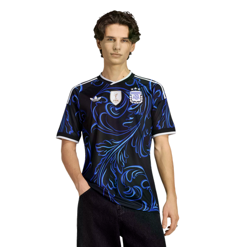 Young man modeling a black Adidas Argentina jersey with a blue swirl pattern, FIFA World Cup champions patch, and AFA crest.