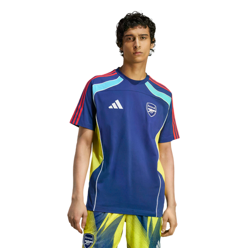 A man wearing a blue Adidas Arsenal F.C. training jersey with yellow accents and matching patterned shorts, standing against a black background.