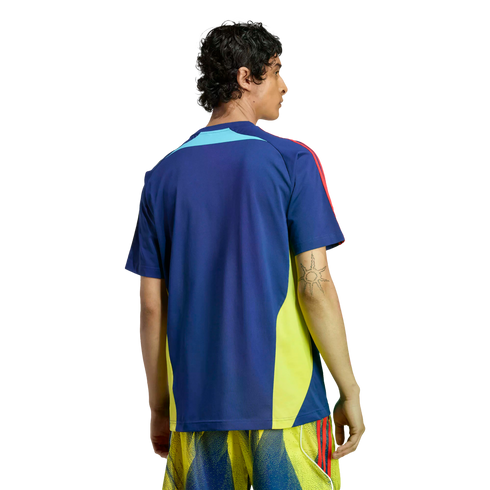 Back view of a man wearing a blue sports shirt with yellow side panels and red shoulder stripes, paired with yellow patterned shorts against a black background.