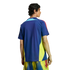 Back view of a man wearing a blue sports shirt with yellow side panels and red shoulder stripes, paired with yellow patterned shorts against a black background.
