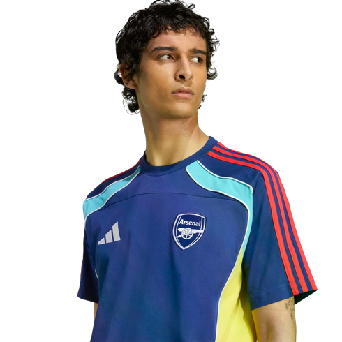 Man wearing a blue Adidas Arsenal training jersey with red, light blue, and yellow accents, looking to the side against a black background.