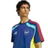 Man wearing a blue Adidas Arsenal training jersey with red, light blue, and yellow accents, looking to the side against a black background.