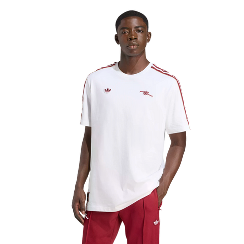 A man models a white Adidas Arsenal T-shirt with red accents and matching red track pants against a plain black background.