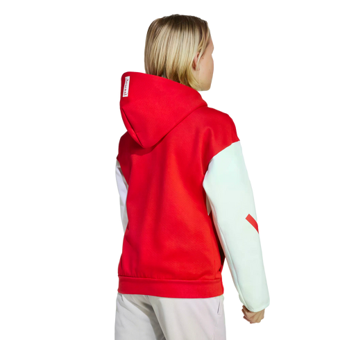 Rear view of a blonde person wearing a red hoodie with white sleeves and light-colored pants against a black background.