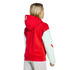 Rear view of a blonde person wearing a red hoodie with white sleeves and light-colored pants against a black background.