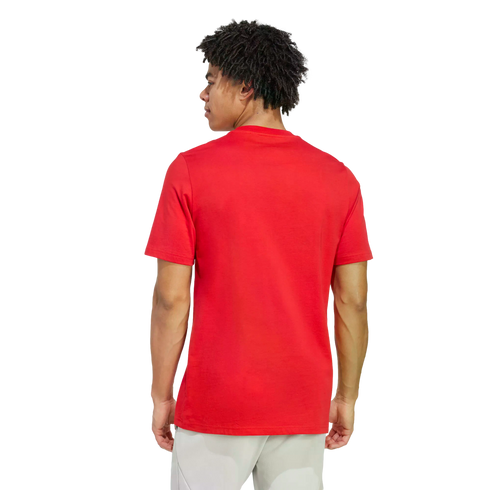 Rear view of a man with dark curly hair wearing a plain red T-shirt and light-colored pants, shown from the waist up against a black background.