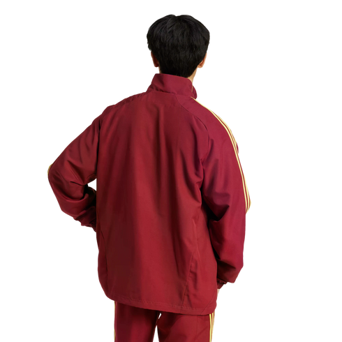 Rear view of a person with short black hair wearing a maroon tracksuit with yellow stripes on the sleeves against a white background.