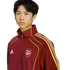 A young person with dark hair wearing a maroon Adidas tracksuit jacket featuring the Arsenal F.C. crest, set against a white background.