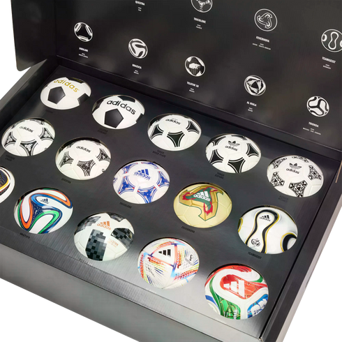A collection of miniature Adidas FIFA World Cup soccer balls showcased in a large black presentation box, featuring iconic match ball designs from various years.