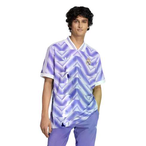 A young man with dark curly hair wearing a purple and white geometric Real Madrid jersey and matching pants against a solid black background.