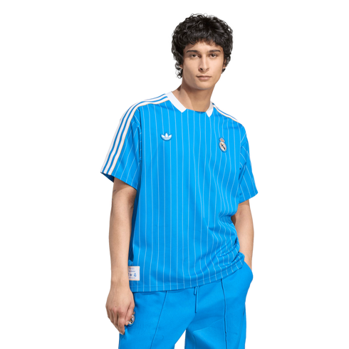 A young man wearing a bright blue pinstriped Real Madrid Adidas jersey and matching pants against a solid black background.