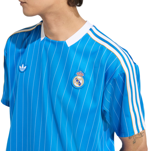 A person wearing a blue Real Madrid soccer jersey with white pinstripes and the Adidas trefoil logo.