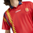 Red Spain Adidas football jersey with a blue polo collar, the national crest, and a vertical yellow and navy diamond pattern on the side.