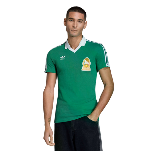 A man models a green Mexico national team soccer jersey with white trim and an Adidas logo against a solid black background.