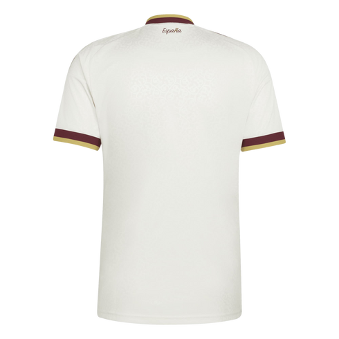 Back view of a white sports jersey with maroon and gold trim on the collar and sleeves. "España" is printed in maroon script on the upper back. The fabric has a subtle tonal pattern.