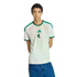 A medium shot of a young man with curly hair wearing an off-white Algeria national team jersey and blue jeans, posed against a black background.