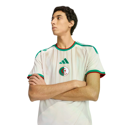 A man with crossed arms wearing an Algeria national team soccer jersey against a black background.