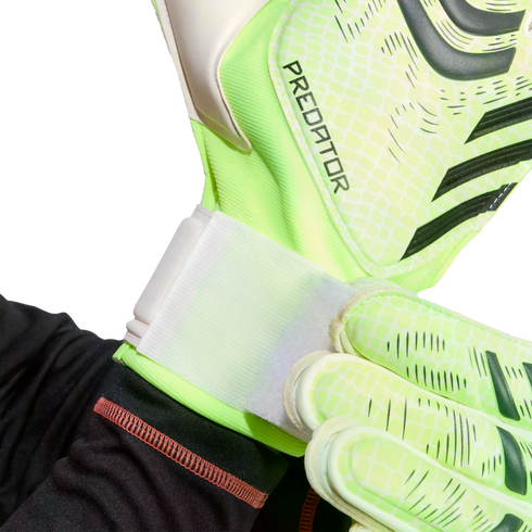 Close-up of a person fastening the white wrist strap of a lime green Predator goalkeeper glove.