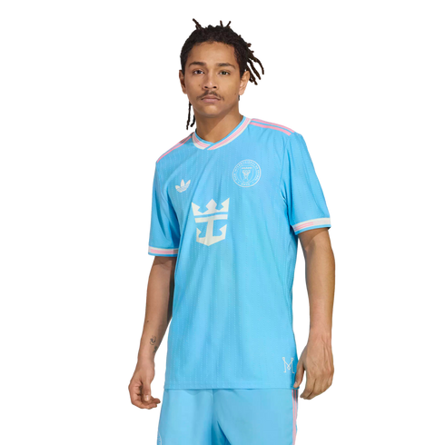 A man with dreadlocks models a light blue Inter Miami CF soccer jersey with pink trim and a Royal Caribbean logo against a white background.