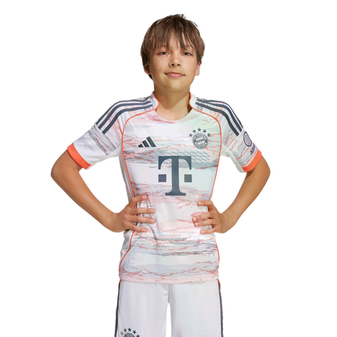 A young boy wearing an Adidas FC Bayern Munich away football kit stands with hands on hips against a white background.