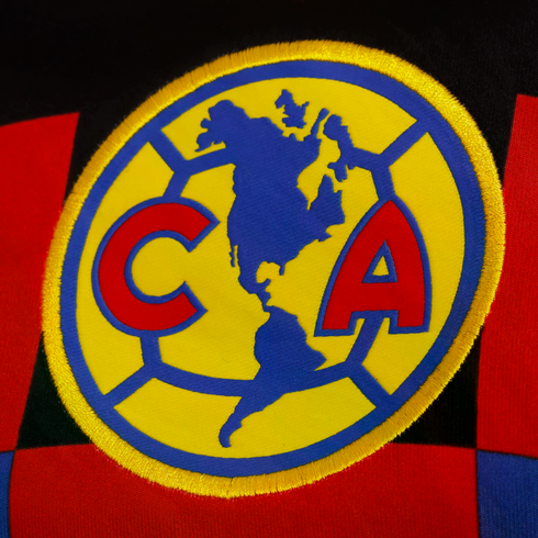 Close-up of the embroidered Club América logo on colorful fabric, featuring a yellow circle with a blue map of the Americas and red letters "C" and "A."