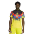 A man wearing a yellow Club América soccer kit with red and blue geometric patterns on the chest and sponsor logos, set against a black background.