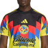A person wearing a Club América soccer jersey with a black, yellow, red, and blue geometric pattern, featuring the team crest and various sponsor logos.