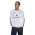 A man wearing a white long-sleeve Manchester United jersey with a Snapdragon logo, looking to the side against a black background.