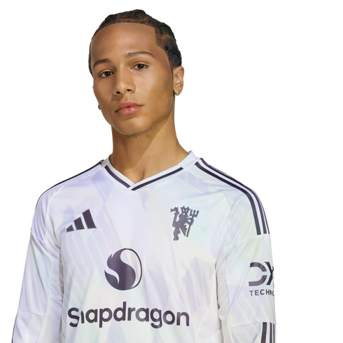 A man in a white Manchester United long-sleeve jersey with a Snapdragon logo, posed against a black background.