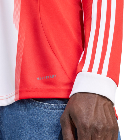 Close-up of a person wearing a red and white long-sleeved shirt with three white stripes on the sleeve, "AEROREADY" branding on the side, and blue denim jeans.