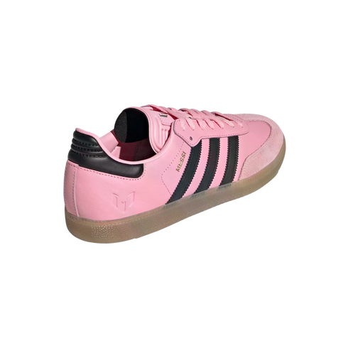 Rear three-quarter view of a pink Adidas Messi Samba sneaker with black stripes and a translucent gum sole against a white background.