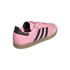 Rear three-quarter view of a pink Adidas Messi Samba sneaker with black stripes and a translucent gum sole against a white background.