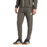 Lower body of a person wearing olive green Adidas track pants and black sneakers with white stripes and gum soles against a black background.