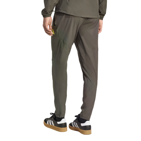 Rear view of a person wearing olive green athletic pants and jacket with black Adidas Samba sneakers.