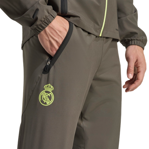A close-up of a person wearing an olive green tracksuit with a lime green Real Madrid crest and zippered pockets.