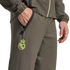 A close-up of a person wearing an olive green tracksuit with a lime green Real Madrid crest and zippered pockets.