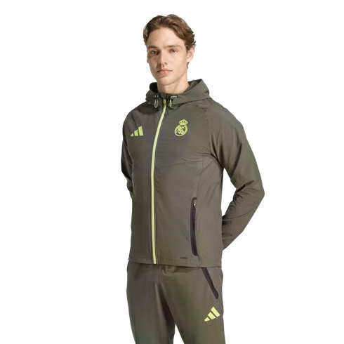 Man in an olive green Real Madrid Adidas tracksuit with neon yellow accents, standing against a black background.