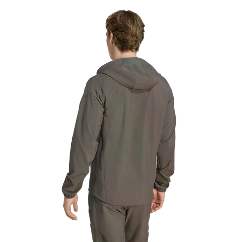 Rear view of a person in a grey hooded windbreaker and matching pants against a solid black background.
