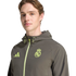 A man wearing an olive green Real Madrid Adidas windbreaker with neon yellow accents, posed against a black background.