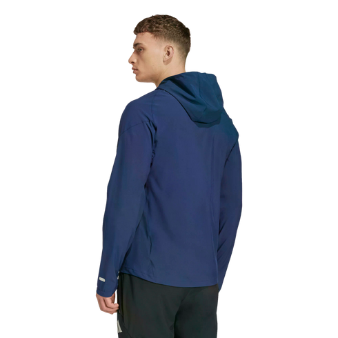 A man is shown from the back and side, wearing a navy blue hooded athletic jacket and black shorts against a solid black background.