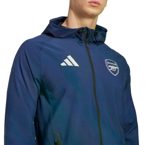 Man wearing a navy blue Adidas hooded jacket with the Arsenal football club crest and white Adidas logo, against a black background.