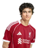 A young man with wavy dark hair wearing a red Liverpool F.C. soccer jersey against a solid black background.