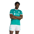 A man models a teal Liverpool FC soccer jersey with white trim and matching white shorts, featuring the Adidas Originals and Standard Chartered logos against a black background.