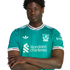 A young Black man with arms crossed wearing a teal Liverpool FC soccer jersey against a black background.