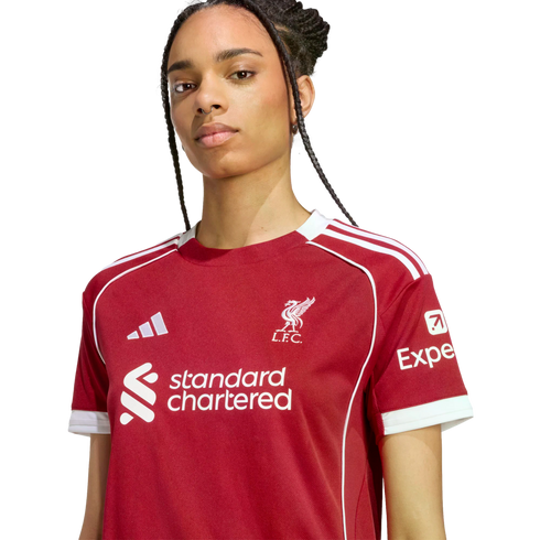 A woman wearing a red Liverpool F.C. football jersey with white trim and sponsor logos, facing forward against a black background.