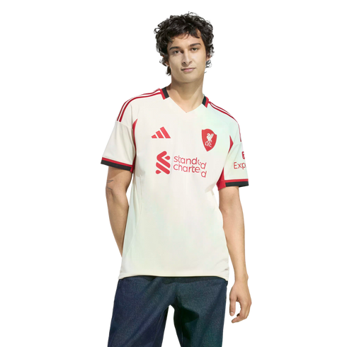A young man wearing a white and red Adidas Liverpool F.C. soccer jersey and blue jeans, standing against a solid black background.
