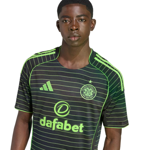 A young Black man wearing a black and neon green striped Celtic FC away jersey against a black background.