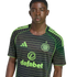 A young Black man wearing a black and neon green striped Celtic FC away jersey against a black background.