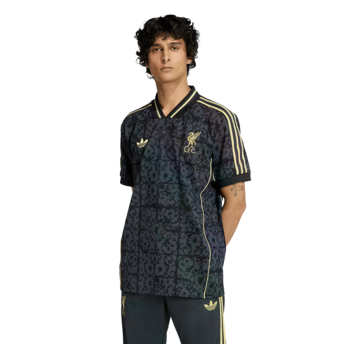 A male model wearing a dark, patterned Liverpool FC x Adidas jersey with gold accents and matching pants against a black background.
